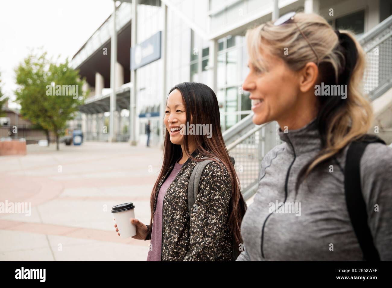 Two women on the move, smiling and talking outside building Stock Photo