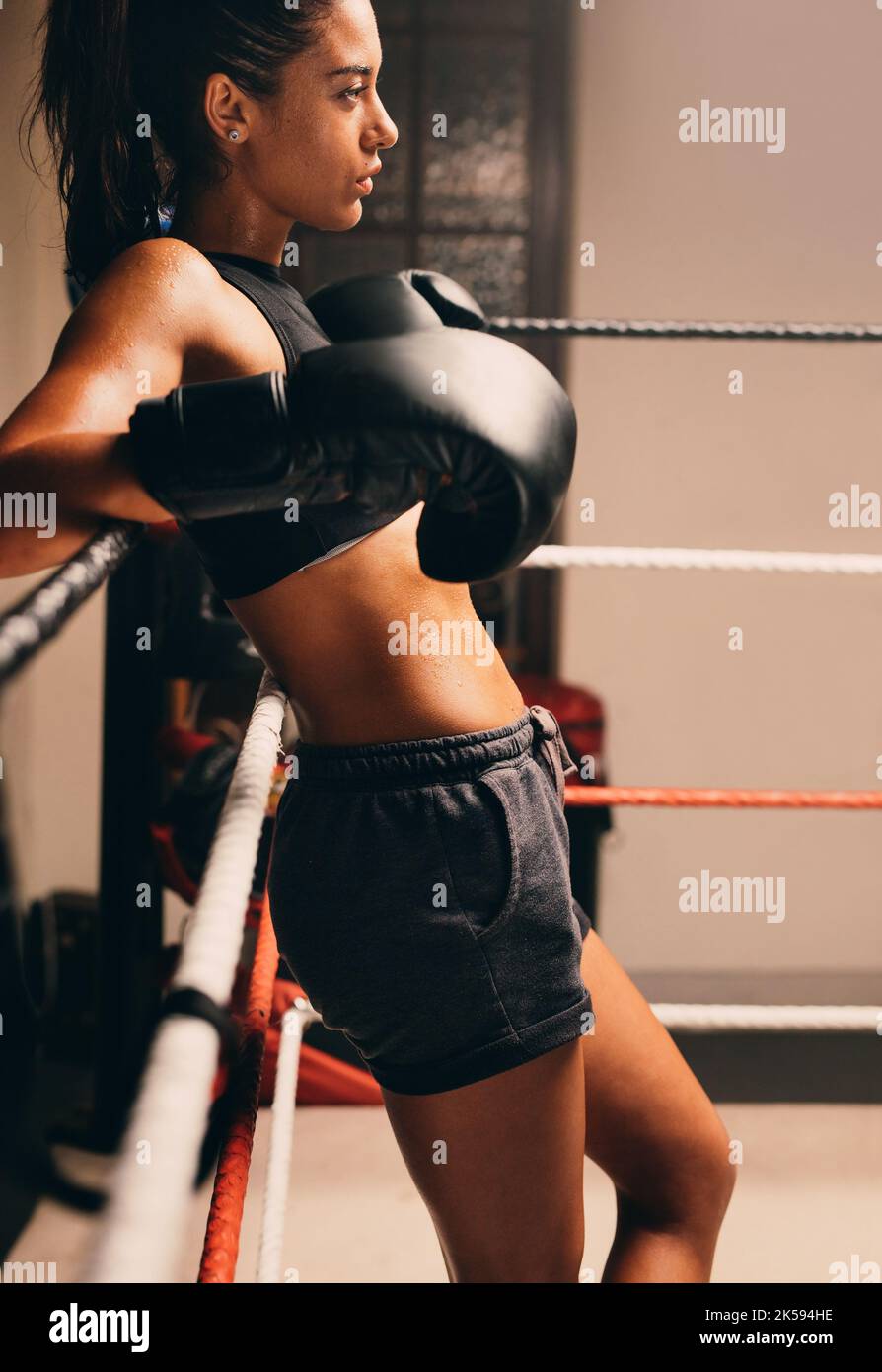 Confident female boxer leaning against the ropes in a boxing ring ...