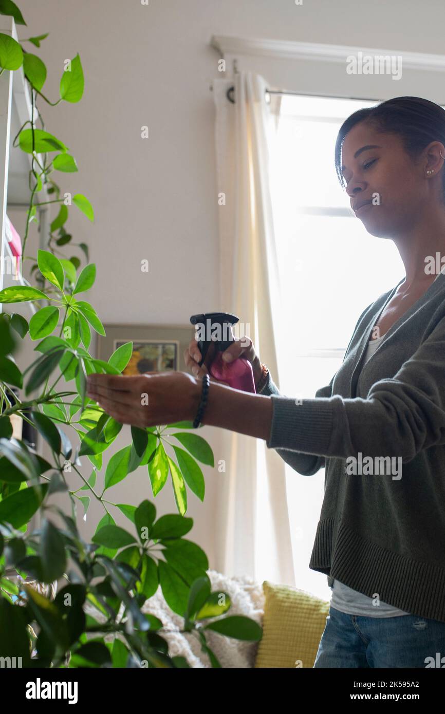 Young woman spraying plant leaves with water in apartment living room