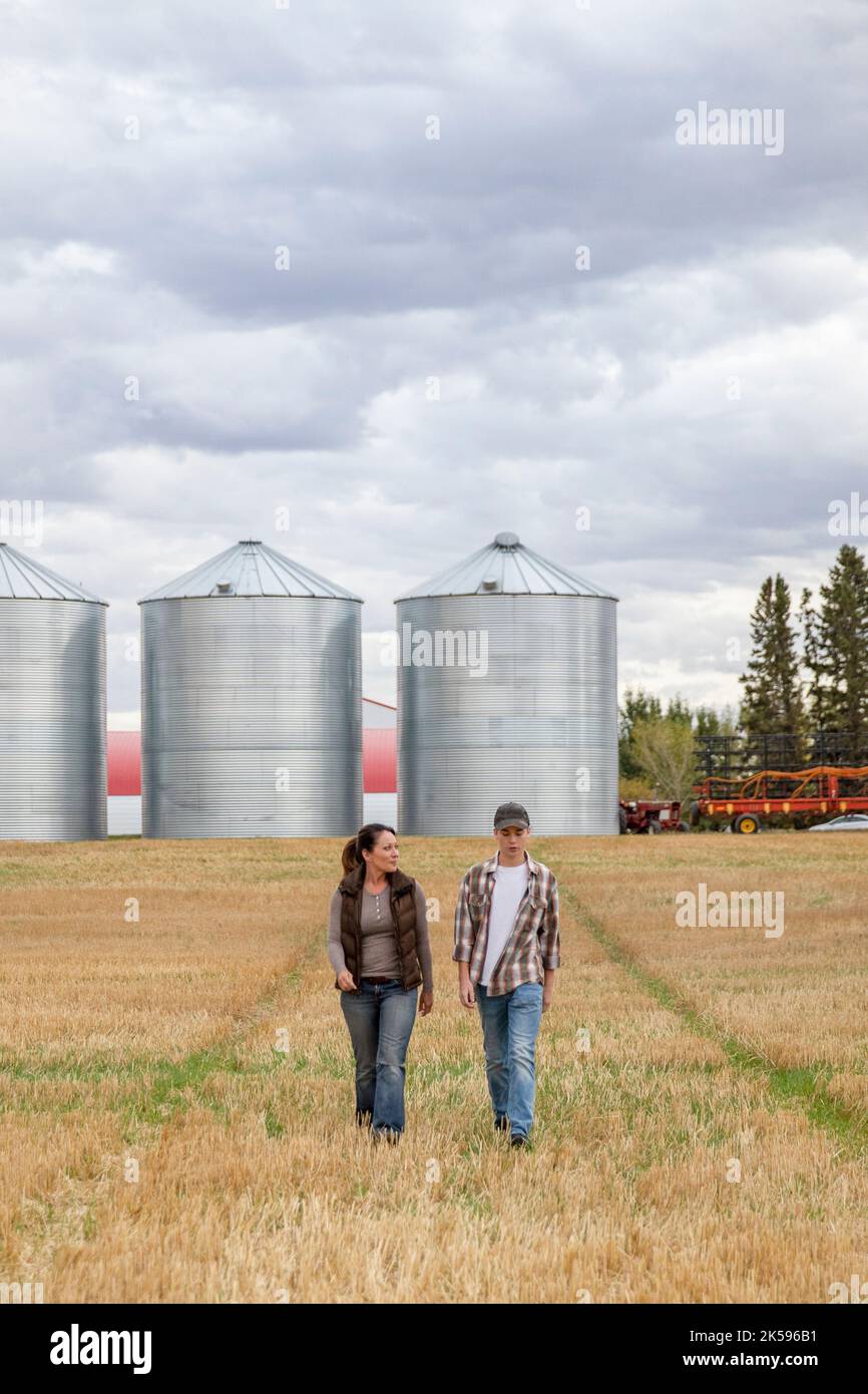 Mother and son farmers walking away from silos in rural field Stock
