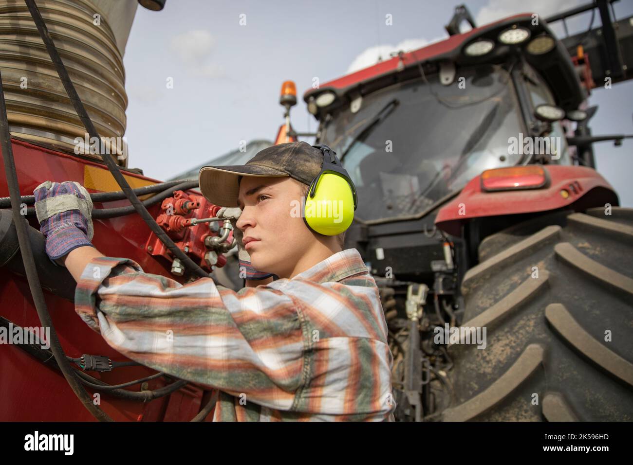 Teenage boy farmer with ear protectors standing at tractor, operating machinery Stock Photo