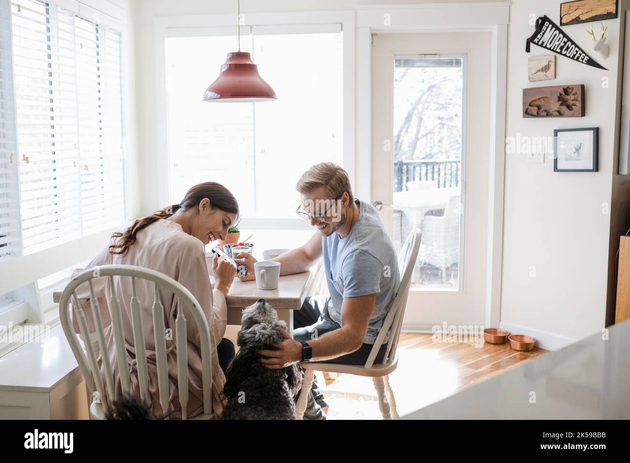 Couple stroking family pet dog at breakfast table Stock Photo