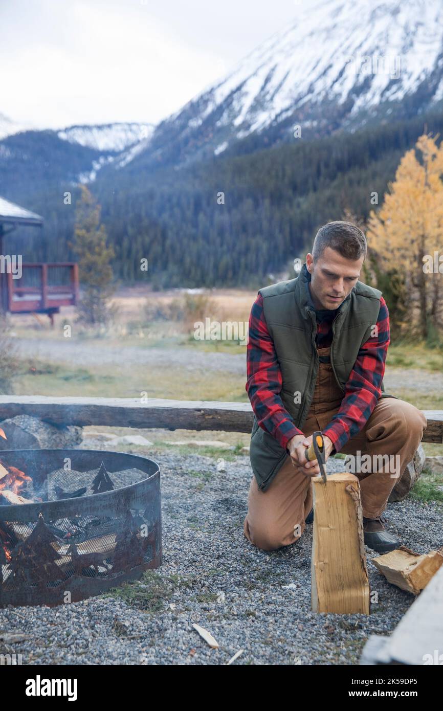 Man splitting firewood for campfire outside mountain cabin Stock Photo