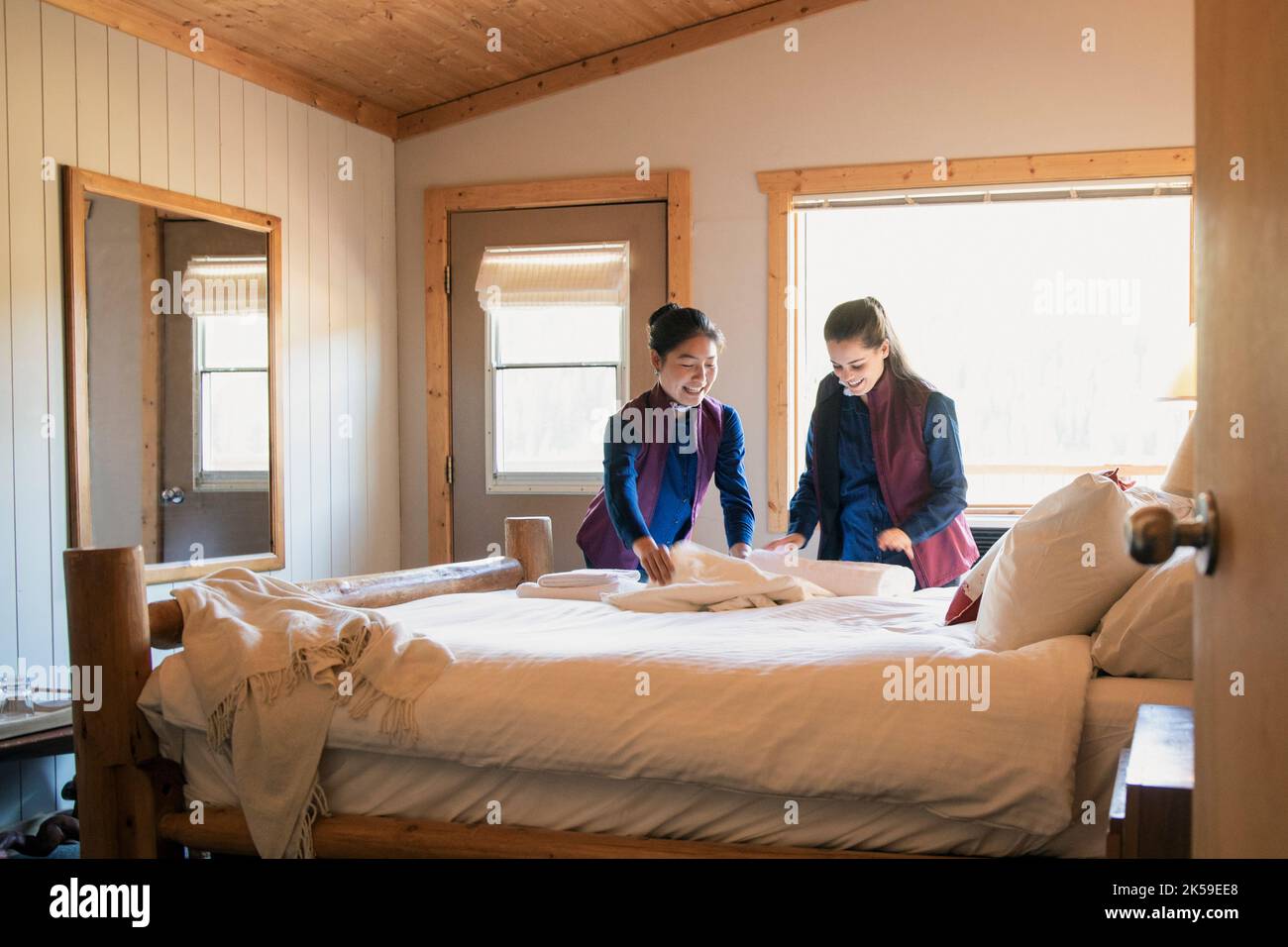 Female hotel employees preparing linens on lodge bed Stock Photo