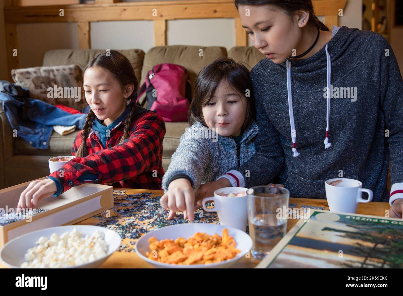 Brother and sisters snacking and assembling jigsaw puzzle Stock Photo