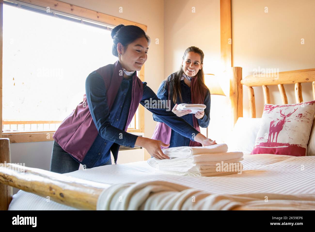Female hotel employees preparing linens on lodge bed Stock Photo