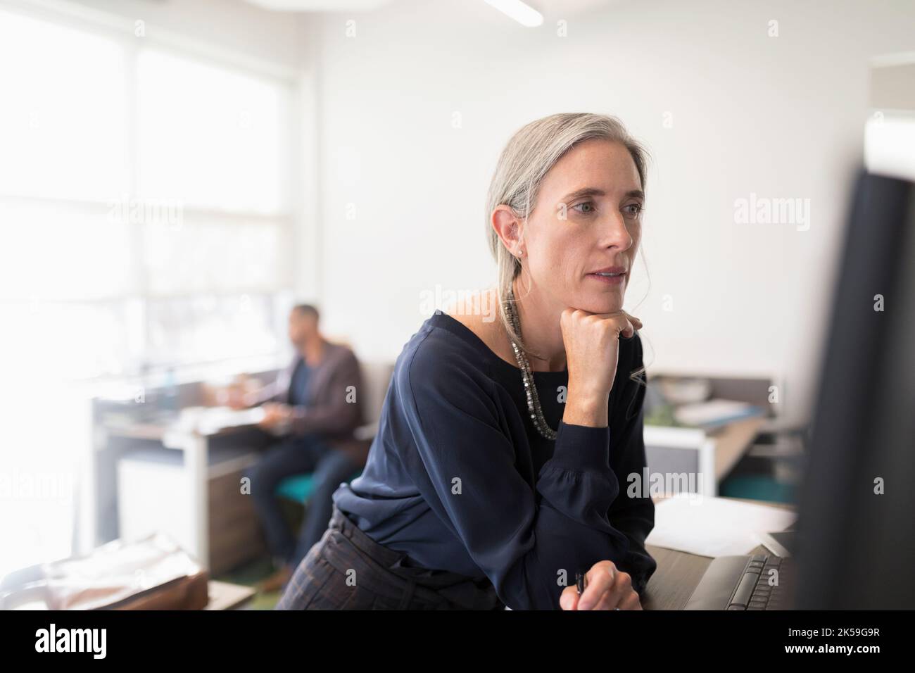 Female manager with hand on chin looking at computer Stock Photo