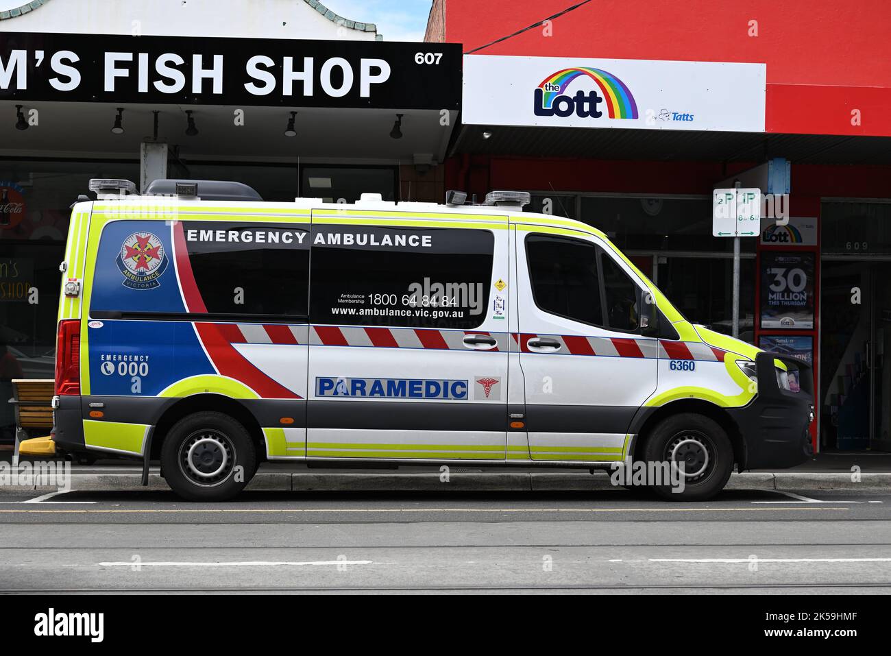 Side view of an Ambulance Victoria emergency ambulance vehicle parked on the side of a road in a shopping strip, with shops in the background Stock Photo