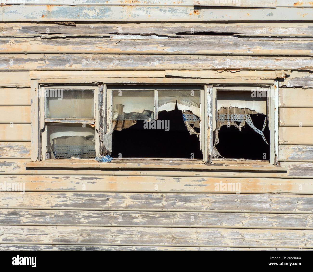 Fraying curtains hang in the windows of an abandoned cottage. Stock Photo