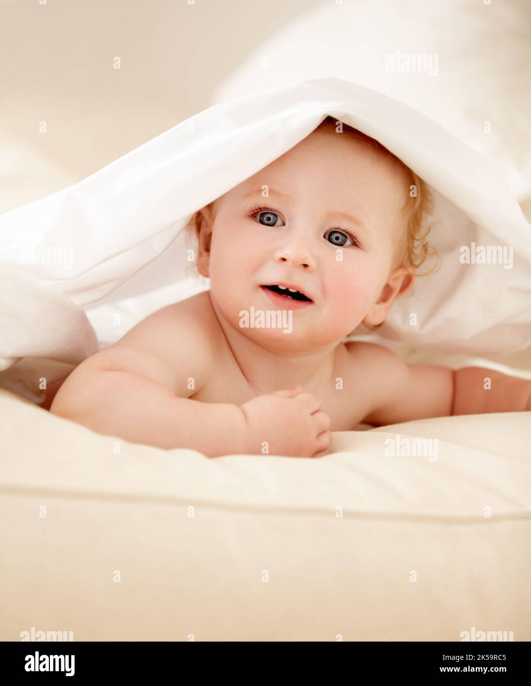 Exploring his world. Cute baby boy lying under a sheet playfully and looking away. Stock Photo