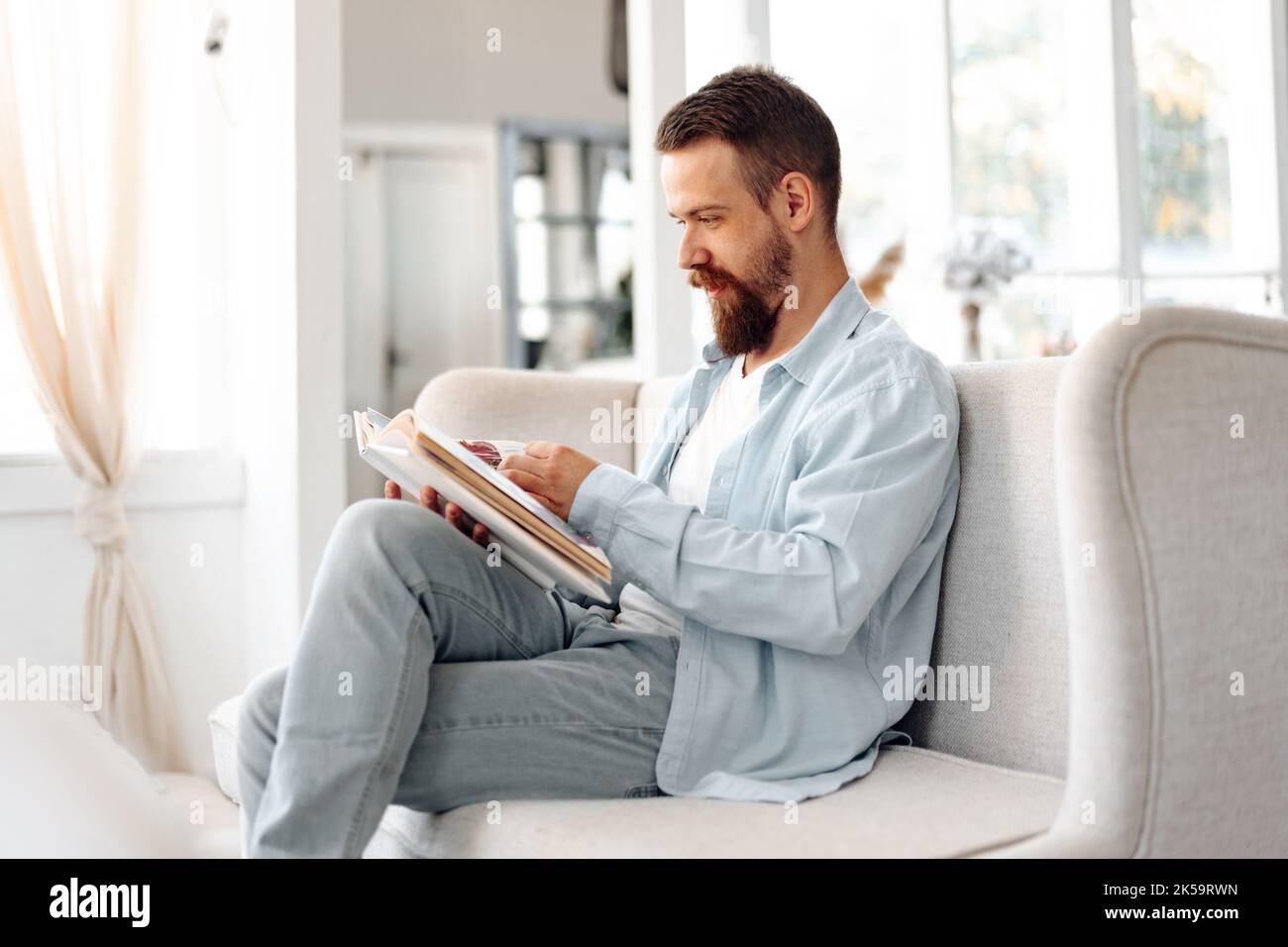 Young bearded handsome man reading book on couch at home Stock Photo ...