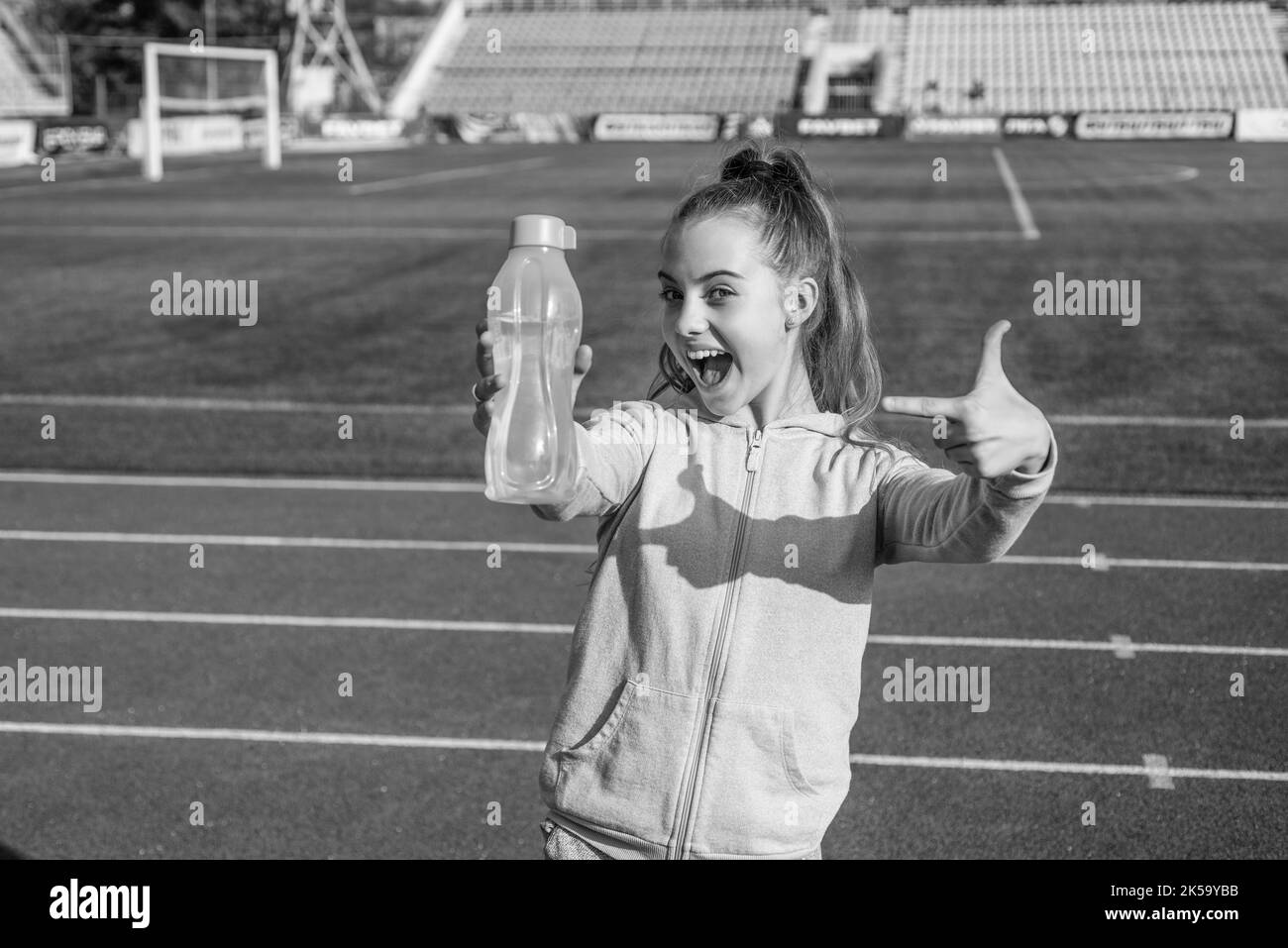 Happy girl child in activewear stand at sports stadium pointing finger