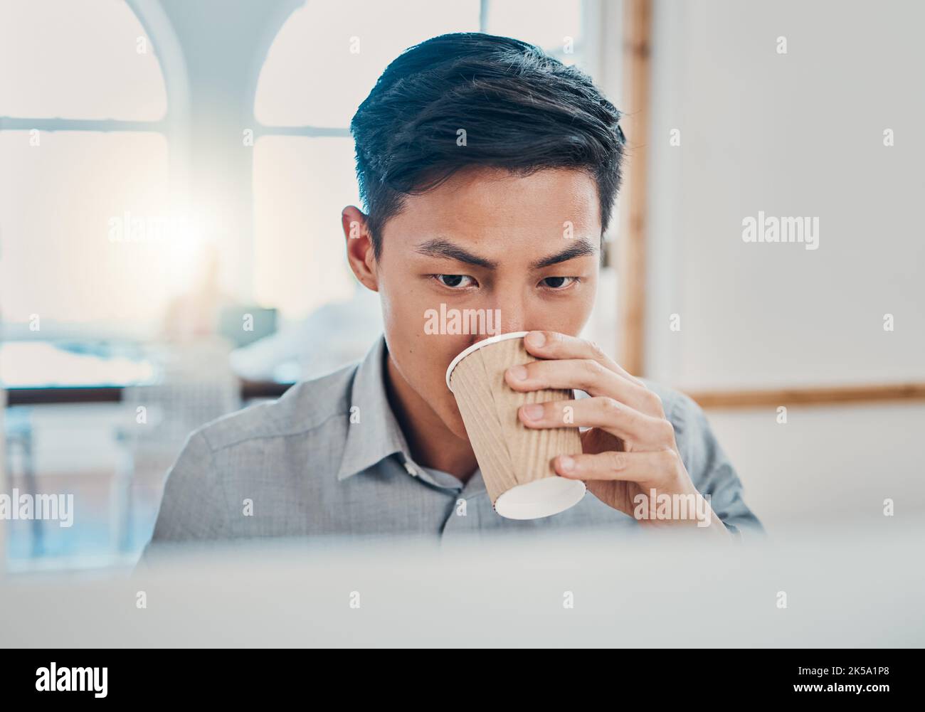 Coffee, computer and commitment with a businessman working in a corporate office for online project. Asian male professional at work on a pc at his Stock Photo