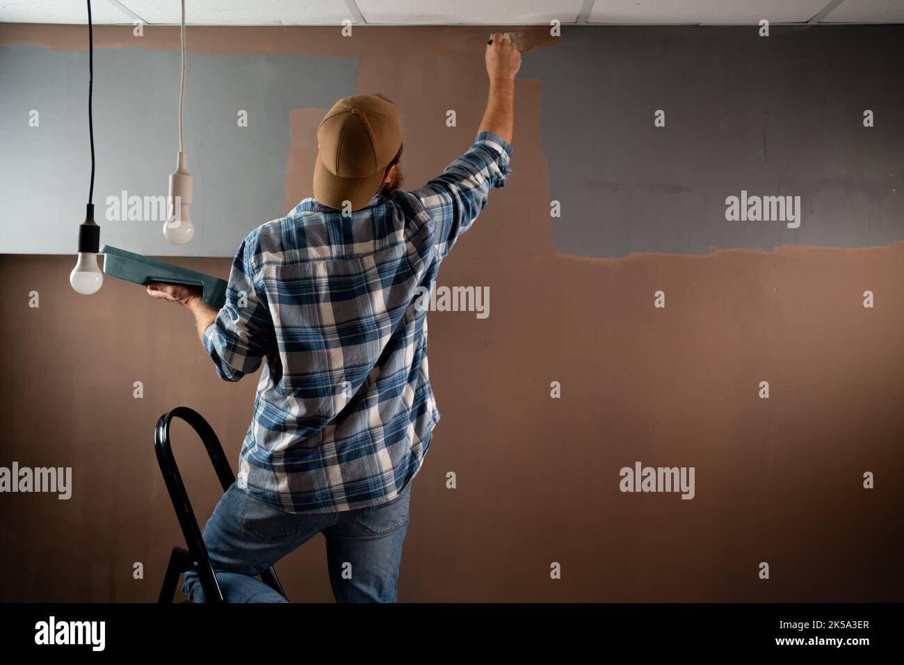 Back view man painter painting the edges of the ceiling with paintbrush
