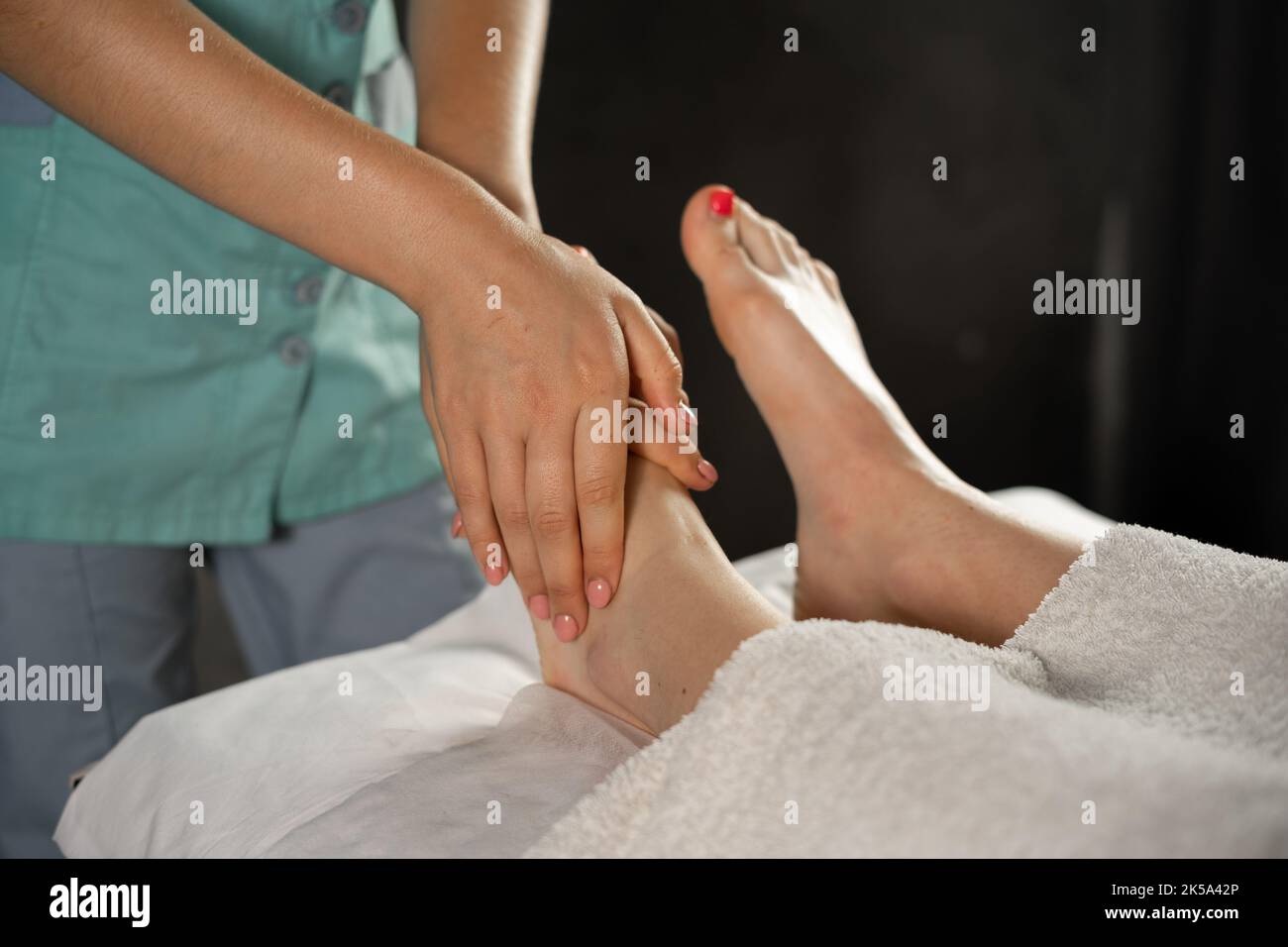 Closeup foot massage in spa salon, beautician undergoing feet massage. Stock Photo