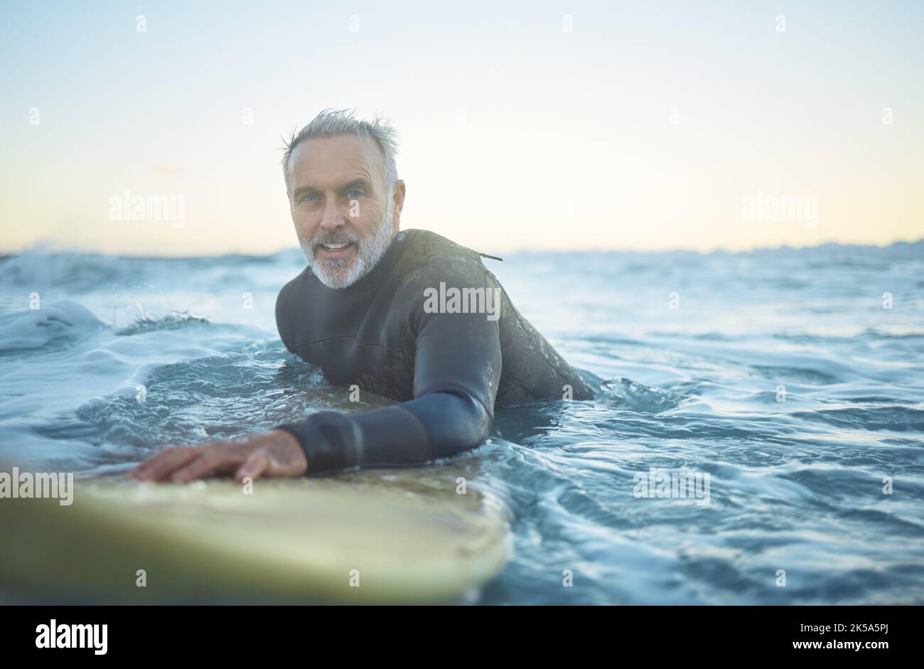 Senior man, surfing in the ocean of Indonesia and free to travel the world in retirement life. Retired surfer, swimming in the sea for fitness and Stock Photo