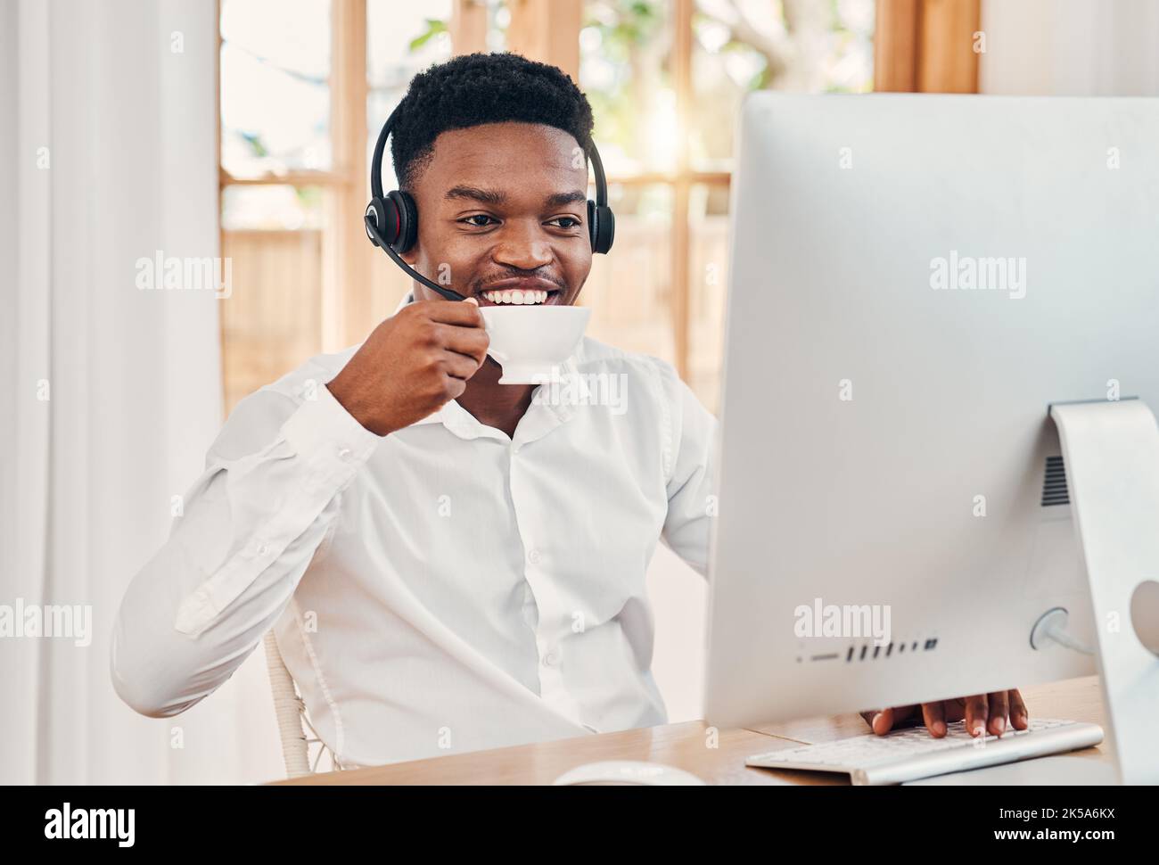 Telemarketing, coffee and customer service employee in call center with headphones at desk. Worker or consultant at table on computer talking to Stock Photo