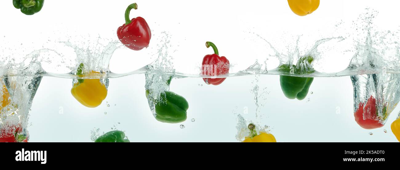Many multi colored peppers splashing in water. Side panoramic view on white background. Stock Photo