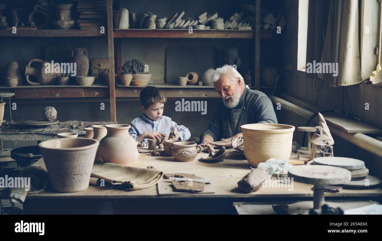 Skilled child is helping his senior grandfather professional potter to