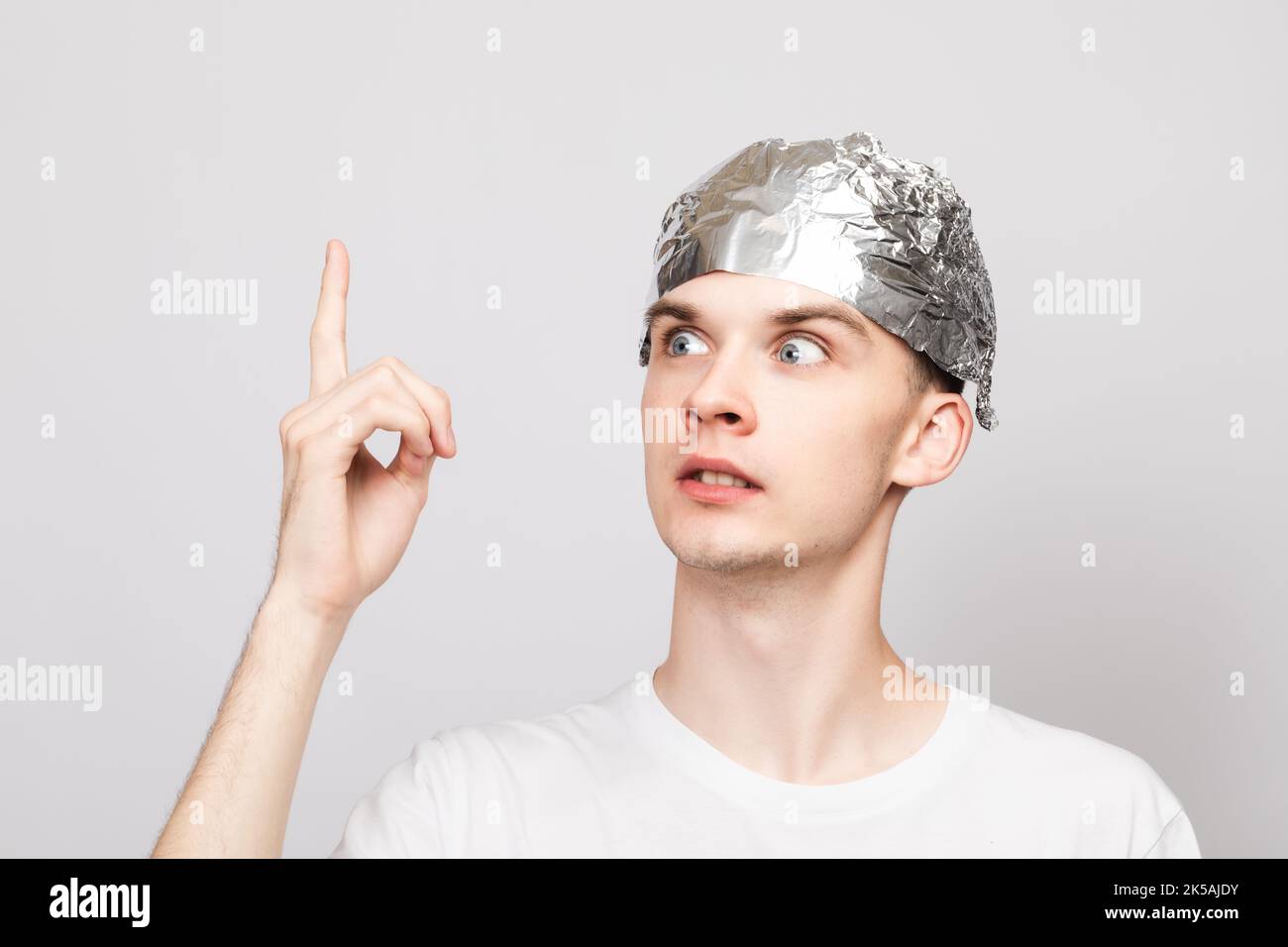 Portrait of crazy young man wearing tin foil hat pointing his finger up