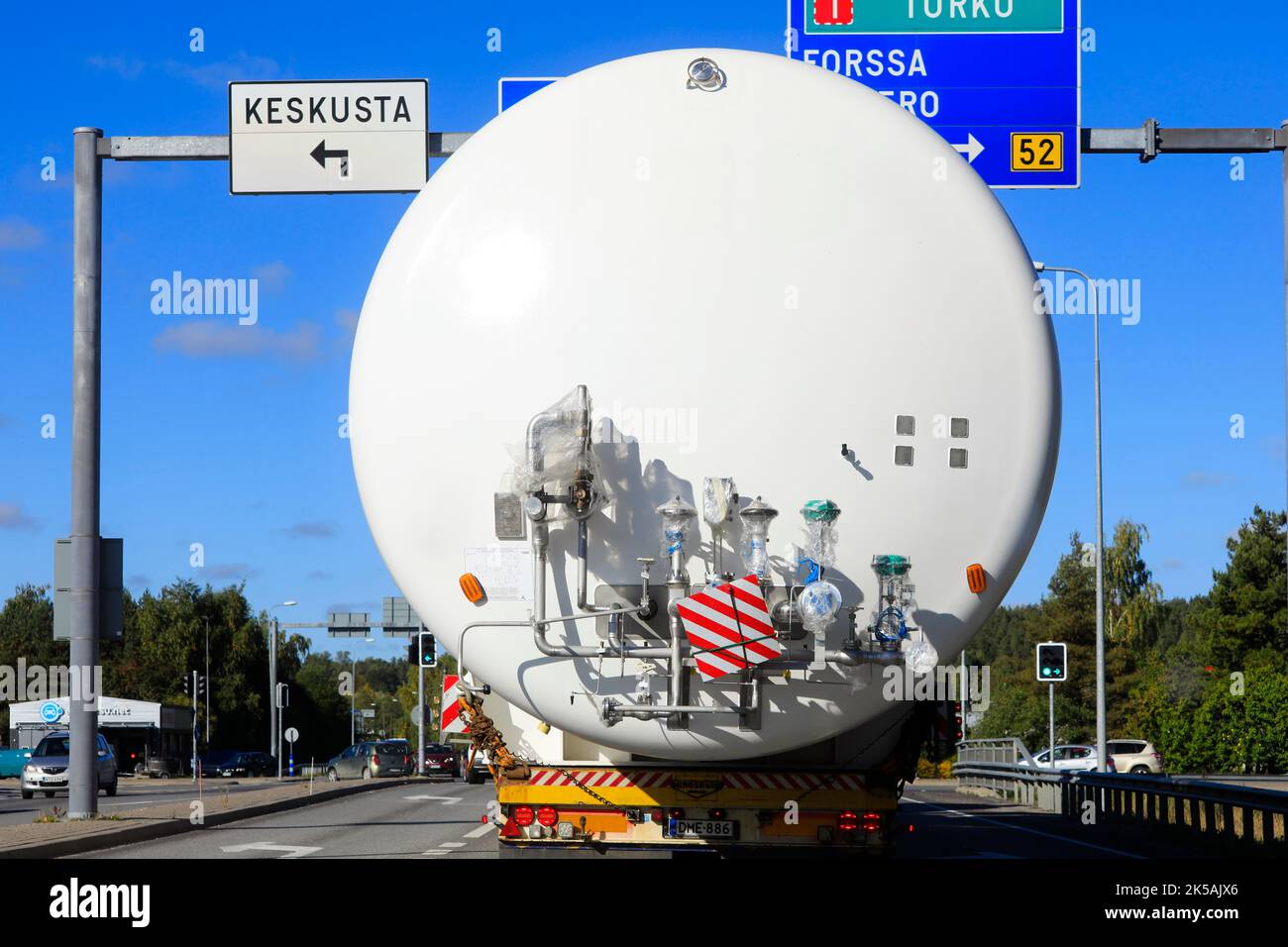 Rear view of oversize load transport of a LNG storage tank approaching intersection with overhead road signs. Salo, Finland. September 22, 2022. Stock Photo