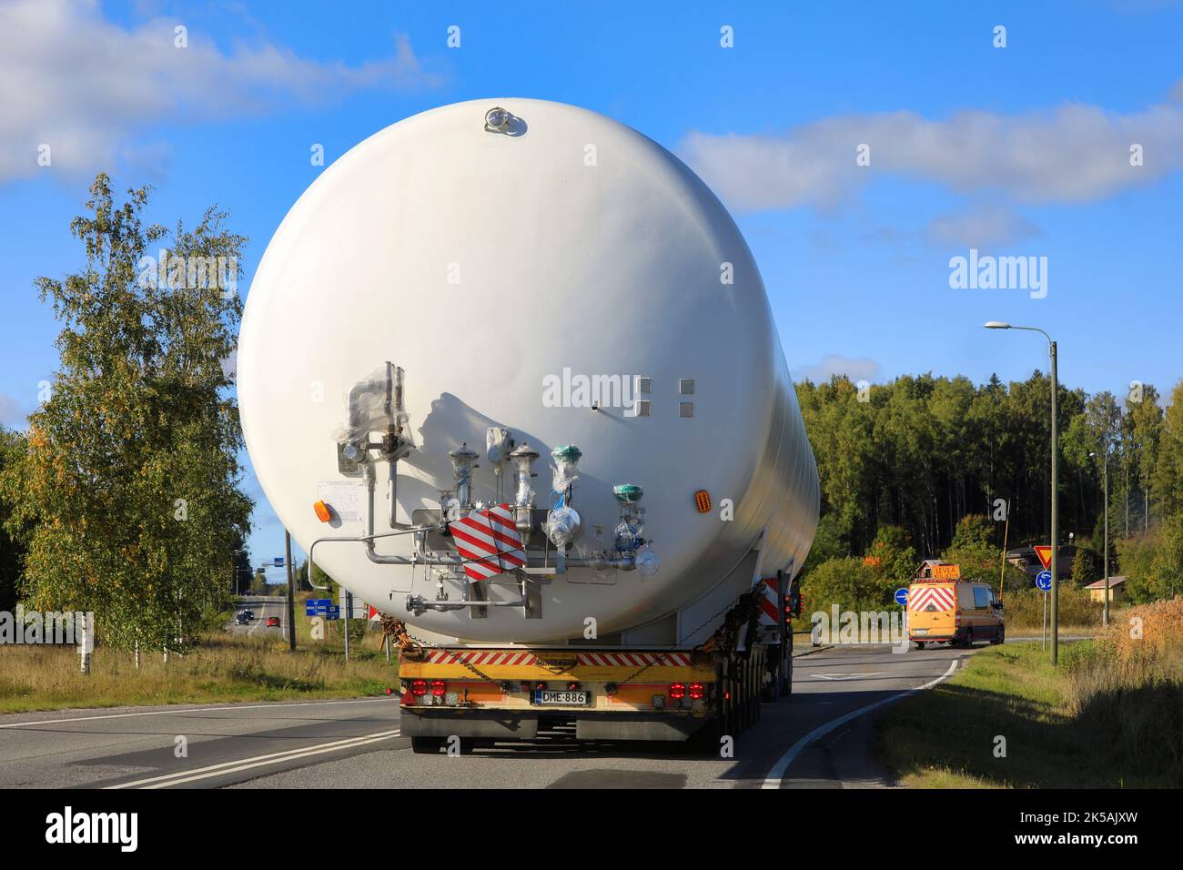 Rear view of oversize load transport of a LNG storage silo in highway traffic, assisted by pilot vehicle. Salo, Finland. September 22, 2022. Stock Photo