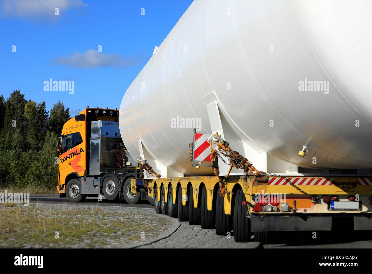 Rear view of oversize load transport of LNG storage tank on Broshuis low loader trailer in roundabout. Salo, Finland. Sept 22, 2022. Stock Photo