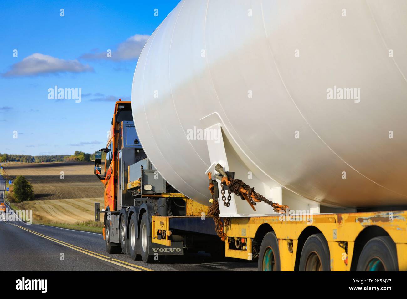 Overtaking yellow Volvo FH16 pulled oversize load of LNG storage tank on highway 110, pilot vehicle leading transport. Salo, Finland. Sept 22, 2022. Stock Photo