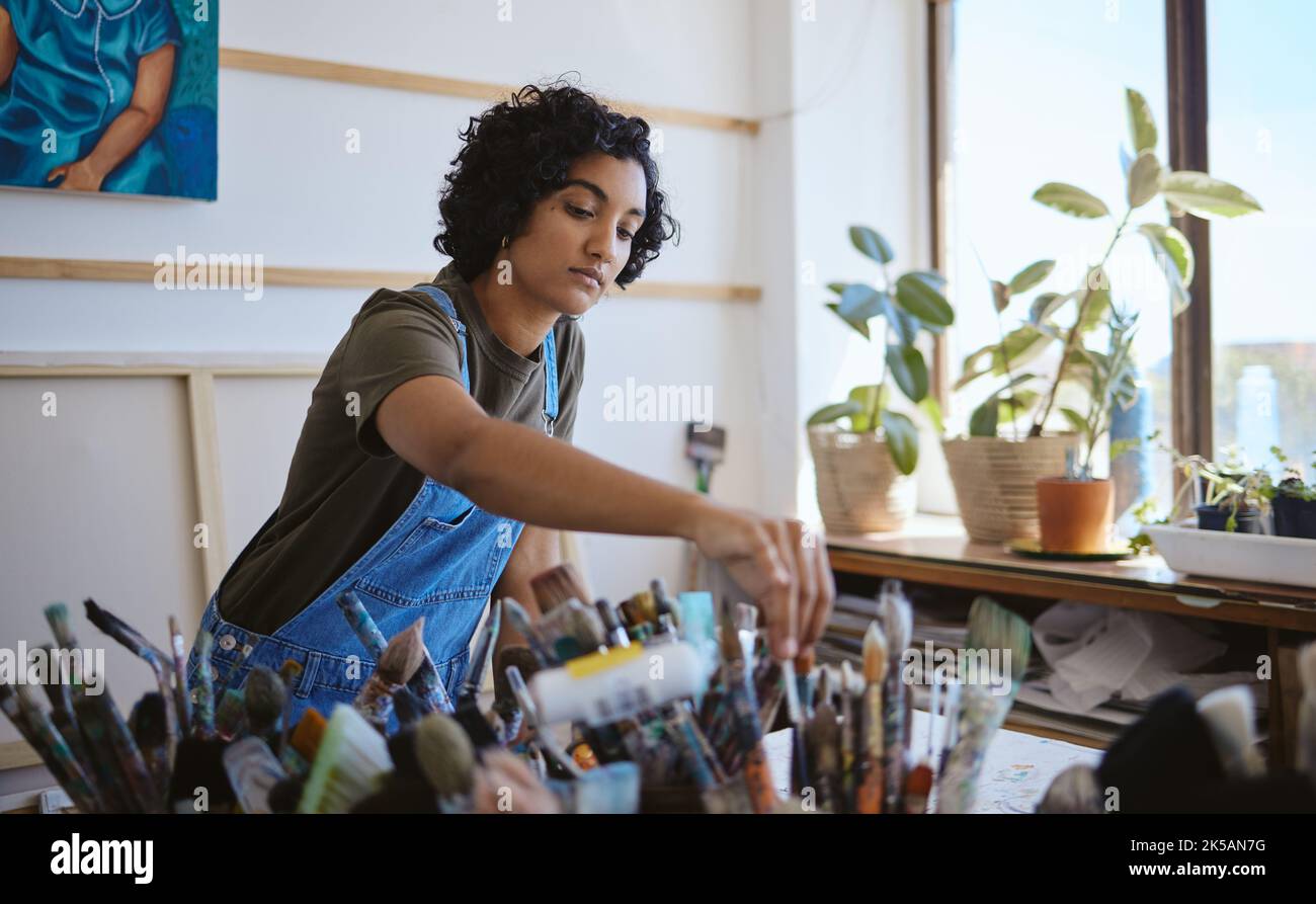 Art, creative and painter with decision for brush while working on a painting in a studio for work. Indian woman, artist or designer picking a tool Stock Photo