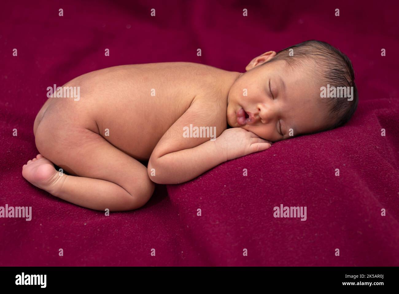 newly born baby laying on red velvet cloth with cute facial expression from different angle Stock Photo