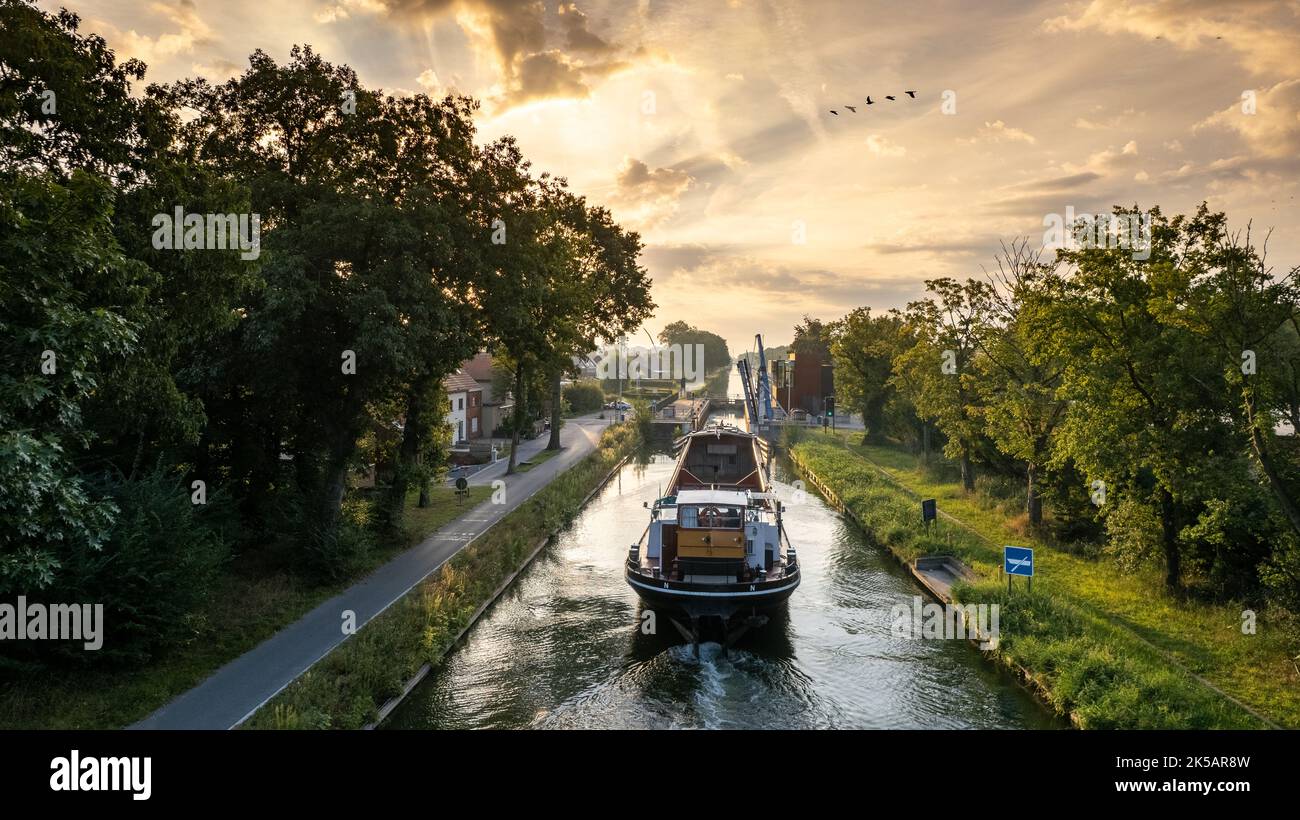 Aerial view of a colourful dramatic sunrise sky over a canal with a cargo boat in Belgium. Canals with water for transport, agriculture. Fields and meadows. Landscape aerial view shot from a drone. High quality photo Stock Photo