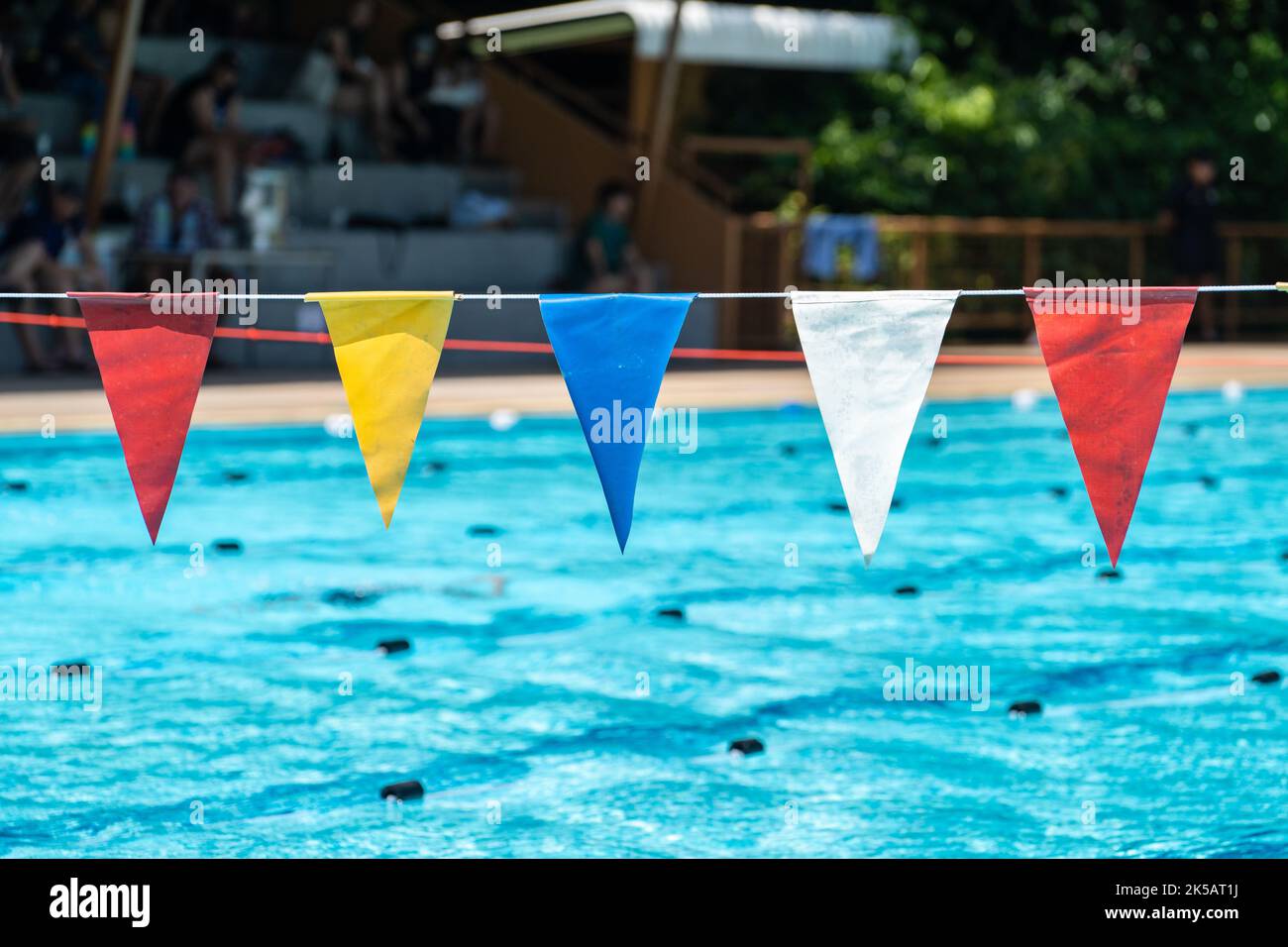 Multicolored triangle swim marker flags hanging above a swimming pool on a bright sunny day
