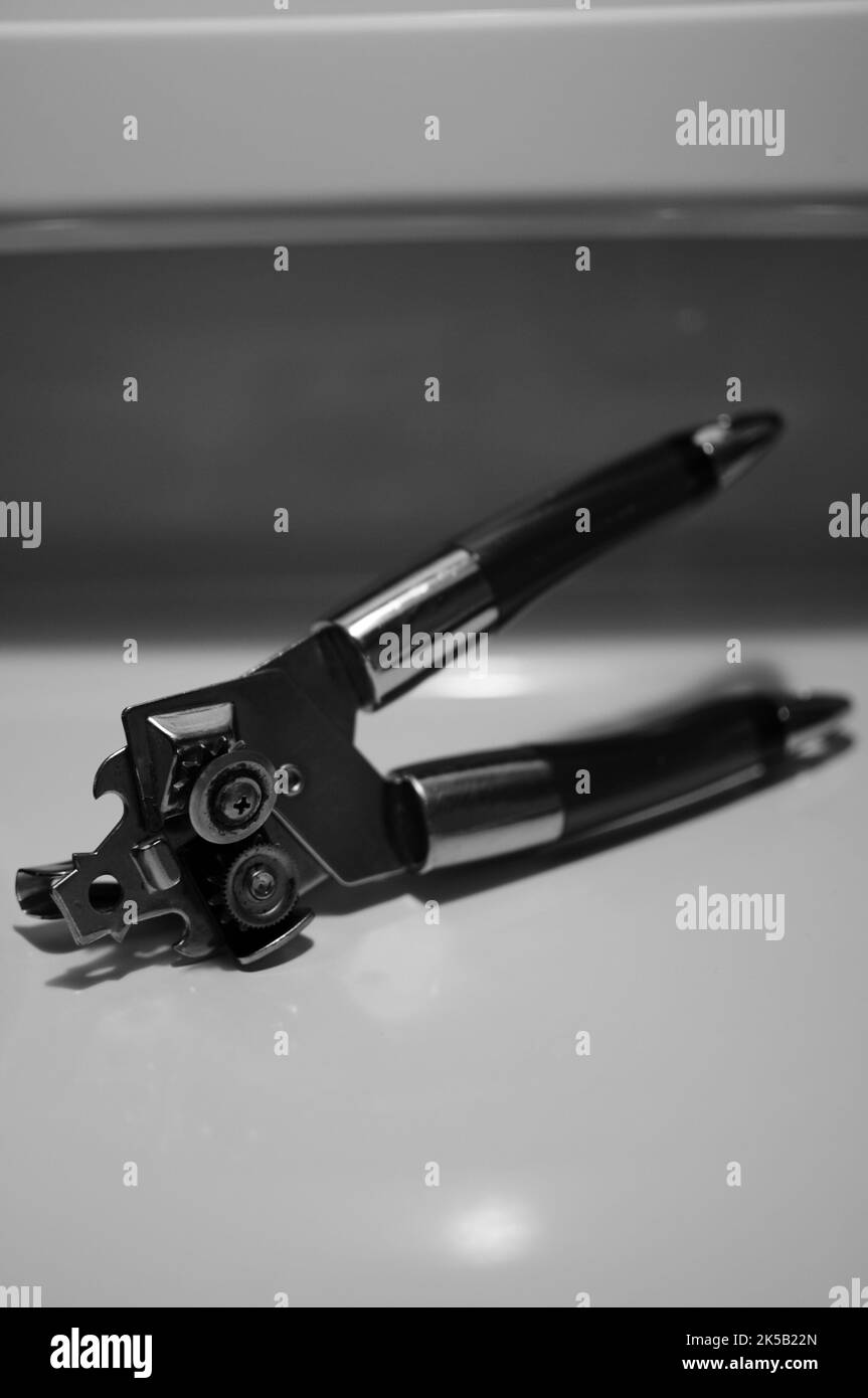 A black and white closeup shot of metal can opener on kitchen table Stock Photo