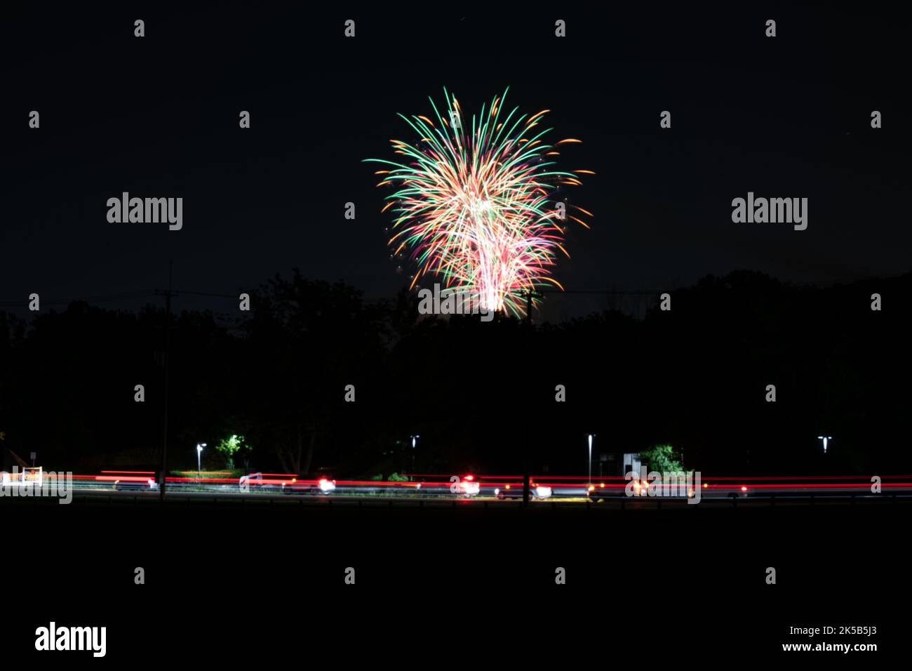 Big colorful fireworks in the night sky with cars driving under Stock