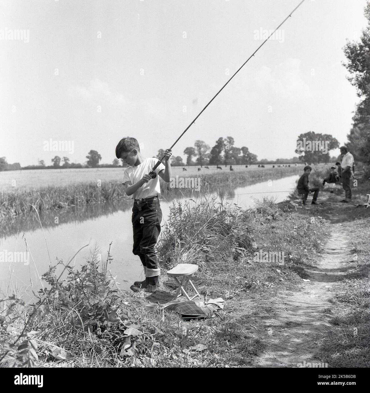 1960s, historical, a young boy with his fishing rod on a riverbank