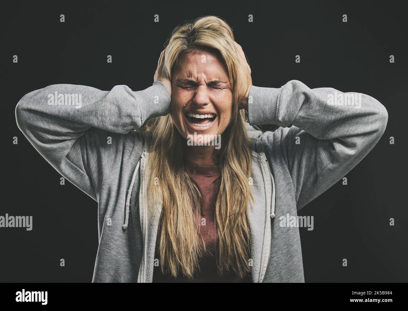Stress, screaming or crying woman with hands over ears on black background in studio with mental health, anxiety or schizophrenia. Psychology Stock Photo