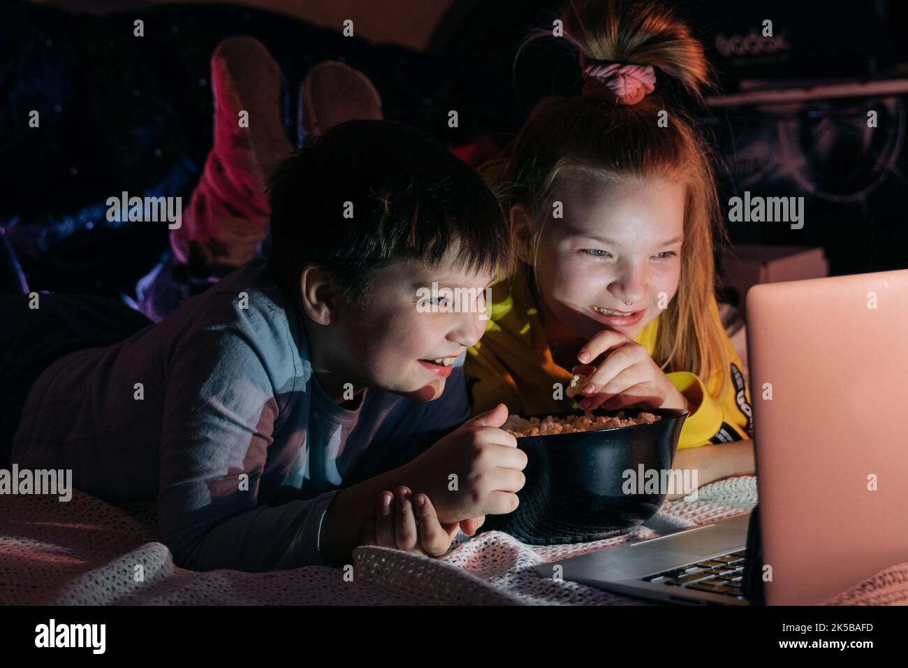 Overjoyed Kids sister brother laughing spend weekend free time together at home on couch bed eating popcorn. teen children watching video cartoon use Stock Photo