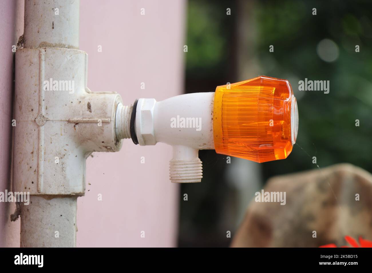 Faucet or plastic water tap with an orange rotating knob fixed on a PVC water pipe attached to a wall Stock Photo