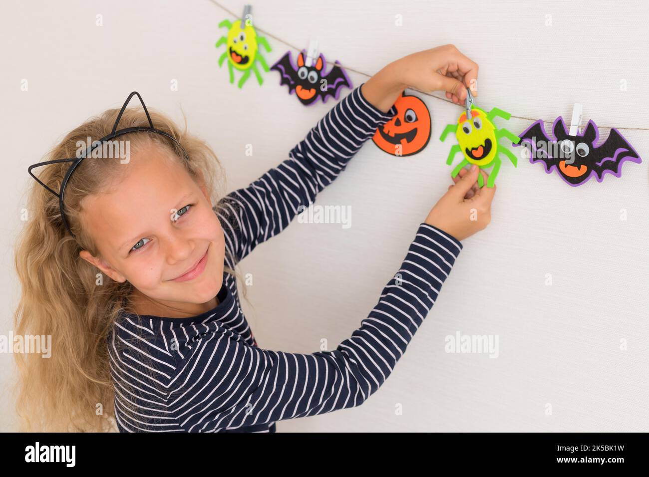 cute little girl preparing for Halloween and hanging monster garland on wall Stock Photo