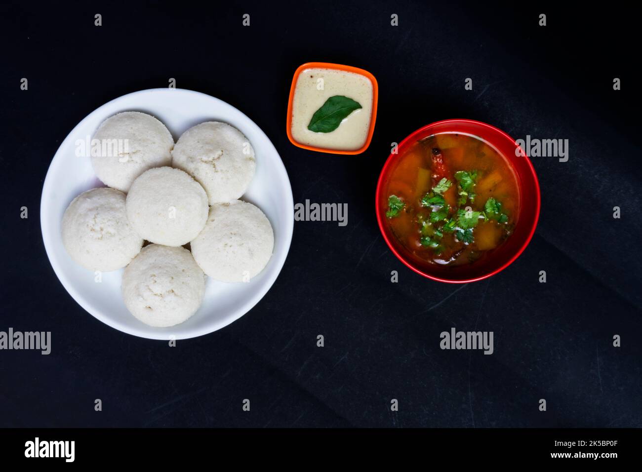 Idly In White Plate, Sambar In Red Bowl with Coconut Chutney In Bowl, Isolated On Black Background, Idly In White Plate, Sambar In Red Round Bowl Stock Photo