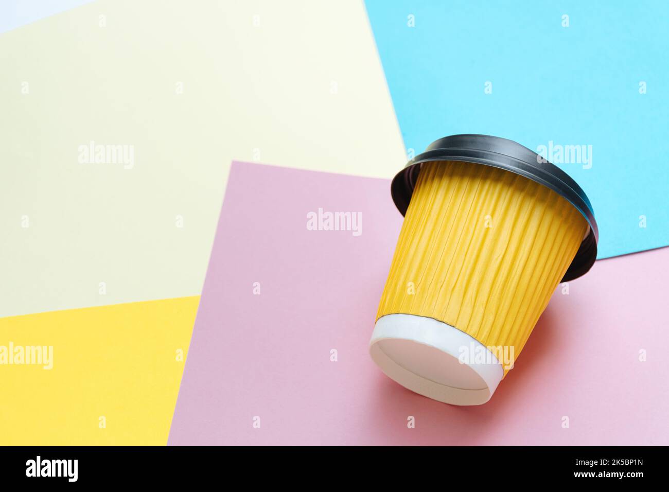 Yellow take-out coffee cup lies in creative mess on colored paper on designer's table. Blue, orange and pink background. Copy Space for text Stock Photo