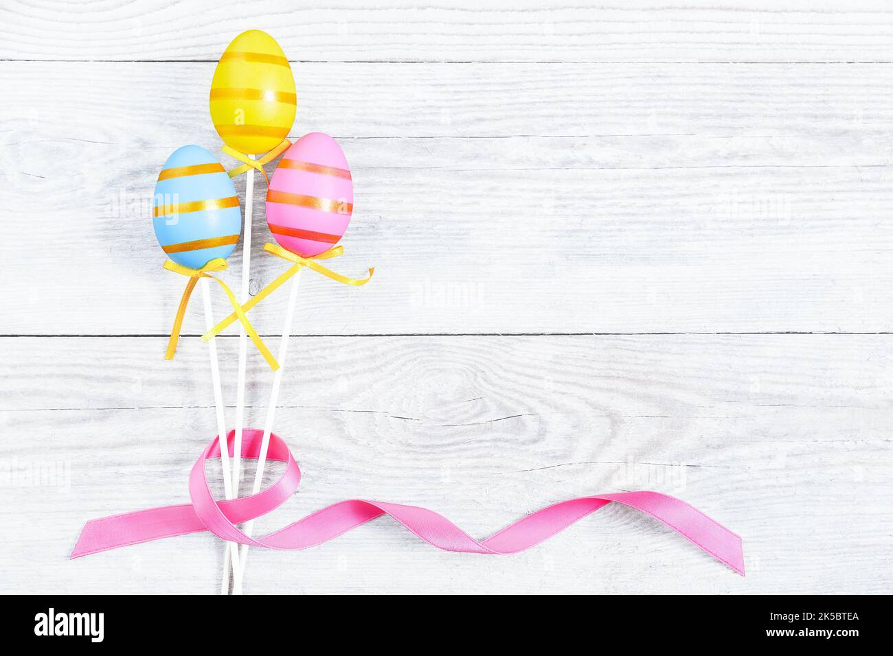 Three colorful Easter egg with pink ribbon bow on blue old wooden table. Light blue Easter background and copy space. Modern greeting card for the cel Stock Photo