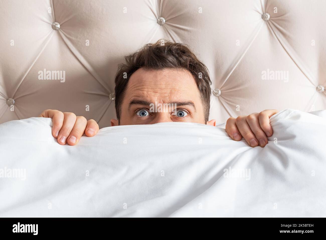 Caucasian young man hiding in bed under the blanket at home. He is stressed and tries run away from problems. Stock Photo