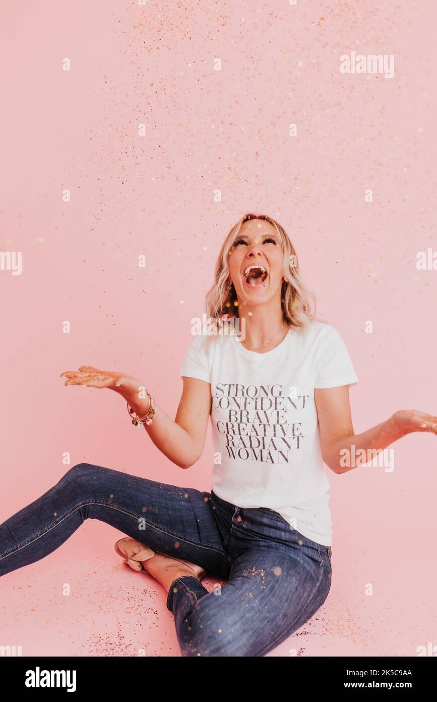 Woman sits on floor laughing after throwing gold glitter Stock Photo