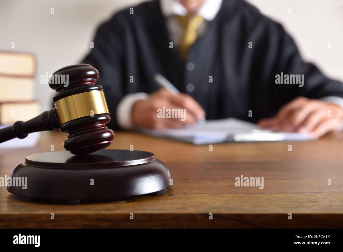 Detail of gavel and judge dressed in the toga signing a document on wooden table. Front view Stock Photo
