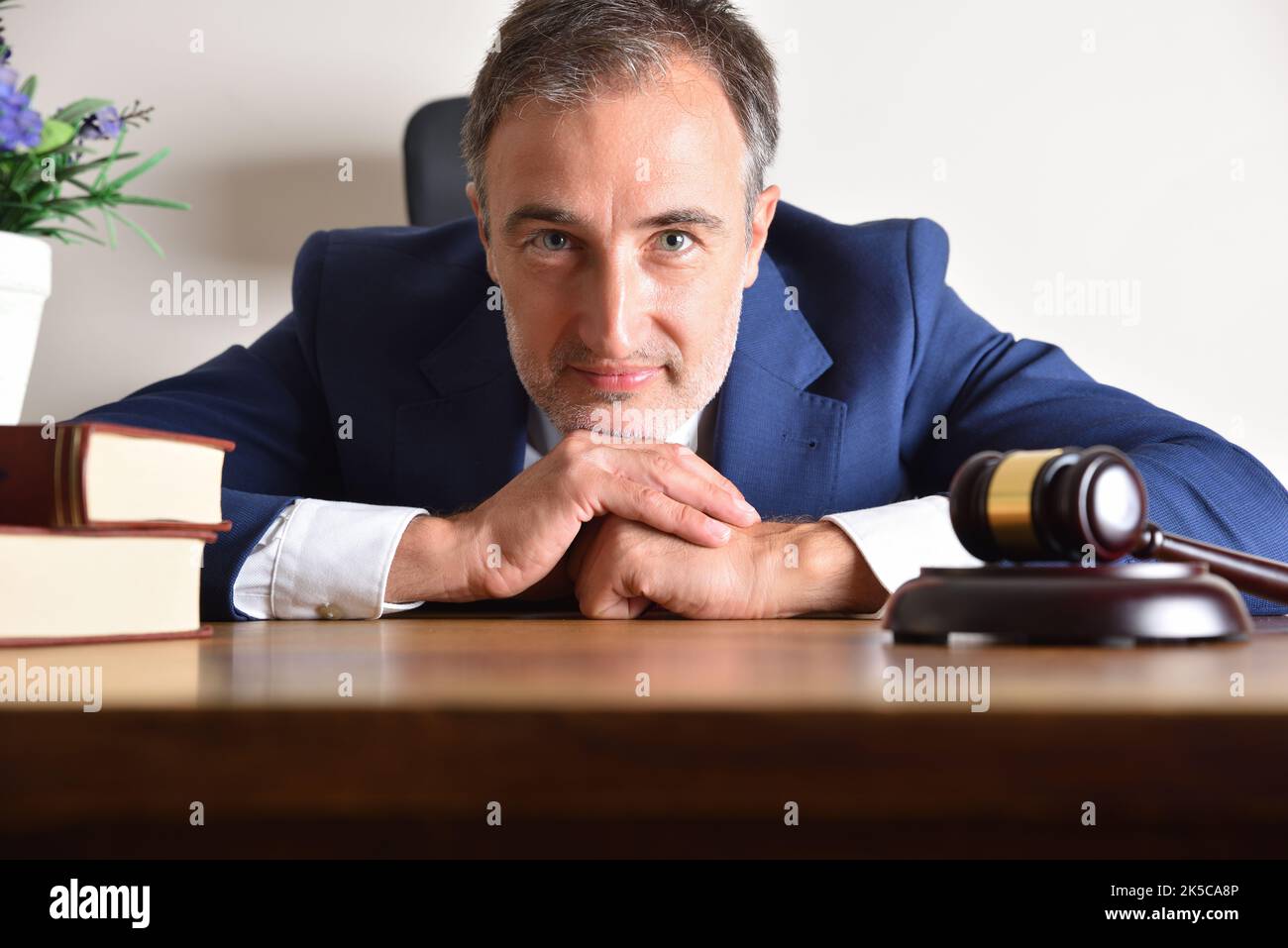 Smiling lawyer in blue suit leaning on his desk with judge's gavel and