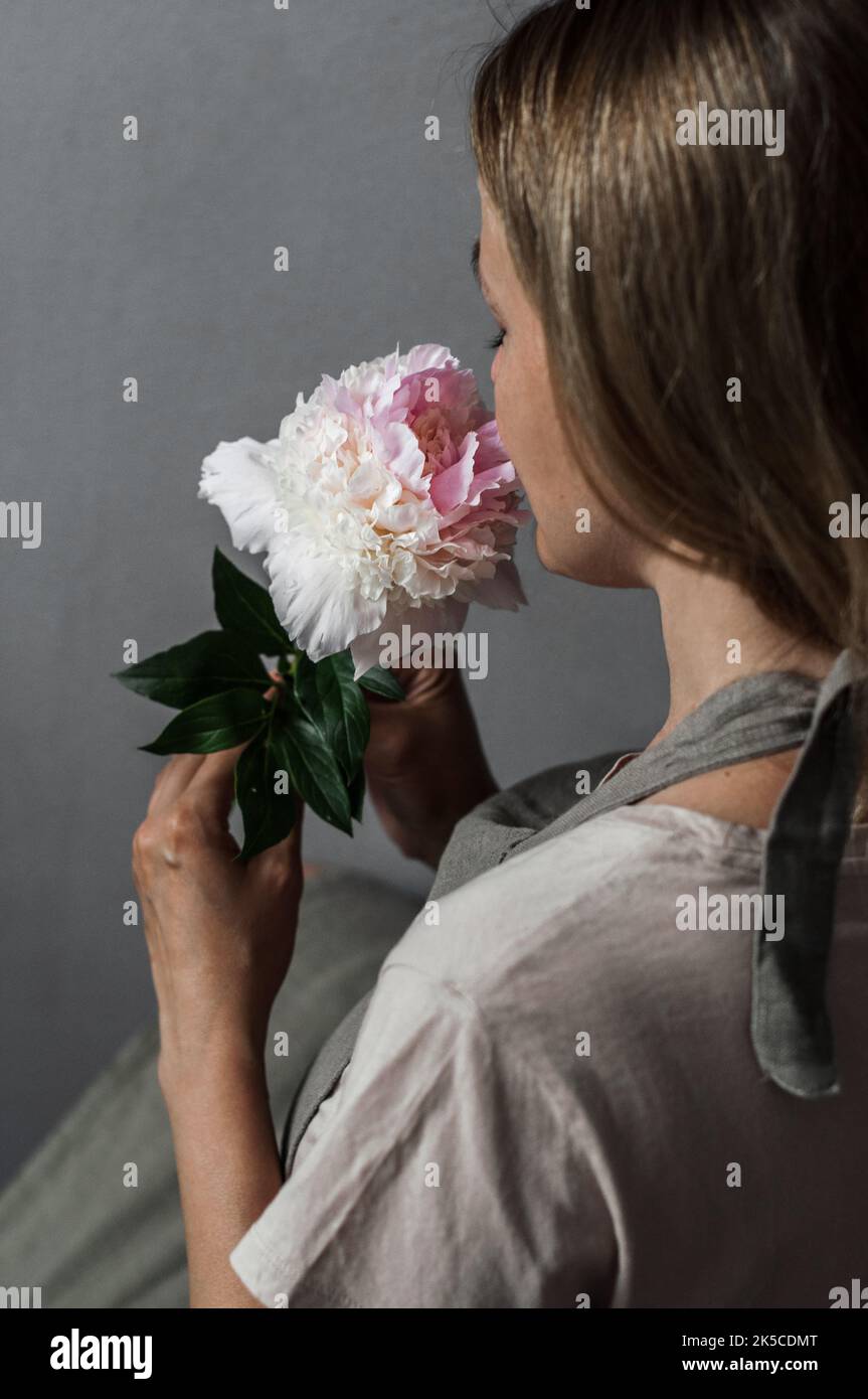 A girl sniffing a peony of the Angel Cheeks variety, half-turned. Stock Photo