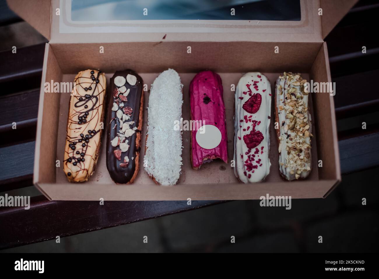 Open box with many colorful Traditional French dessert eclairs and one bite on the bench. Gift concept Stock Photo
