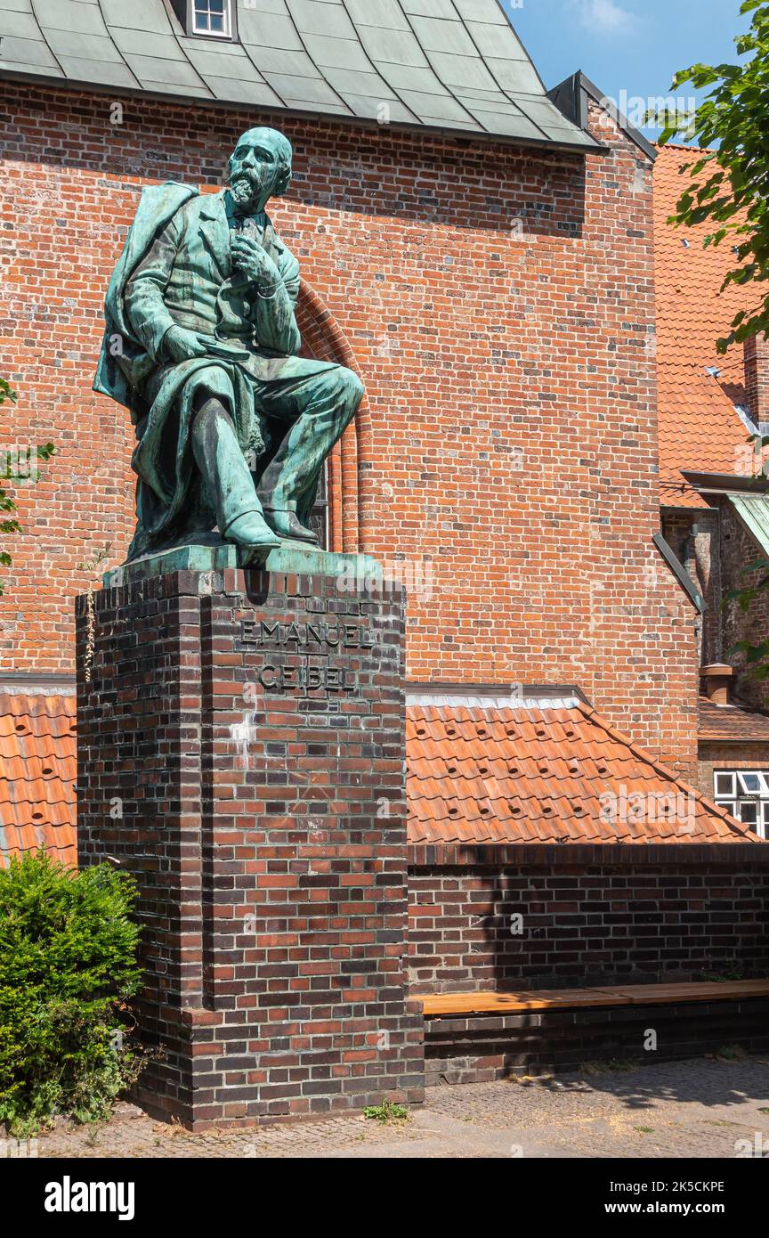 Germany, Lubeck - July 13, 2022: Closeup of poet Emanuel Geibel green bronze statue on brick pedestal  in front of red brick wall at edge of square Stock Photo