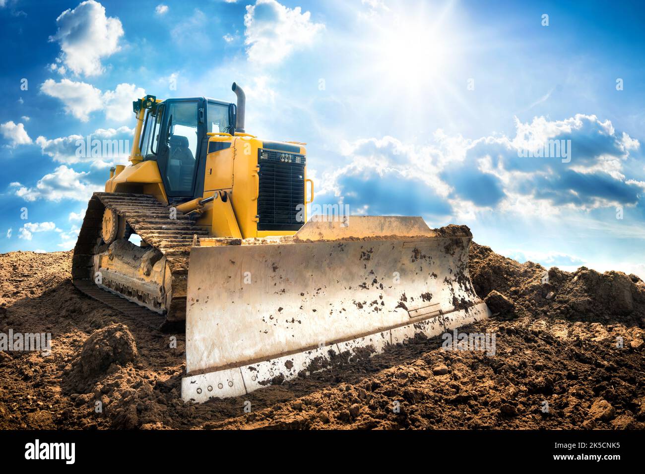 Yellow excavator on dirt, with the bright sun and nice blue sky in the background Stock Photo